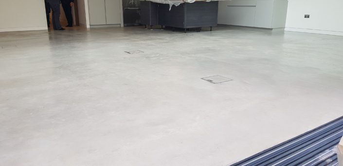 A modern, empty room with a smooth, polished concrete floor—highlighting the elegance discussed in our Polished Concrete Cost in London (2026) | Pricing Guide & Advice—partially open sliding glass doors, and two people standing near a back doorway.