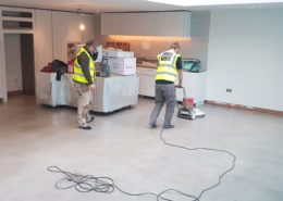Two workers in yellow safety vests use a floor polishing machine on concrete floors. Nearby boxes and equipment hint at ongoing work. Curious about Polished Concrete Cost in London (2026)? Check our Pricing Guide & Advice for details.