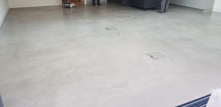 A large indoor space with a smooth, polished concrete floor—an attractive option for those researching Polished Concrete Cost in London (2026) | Pricing Guide & Advice; two people stand near furniture and equipment at the far end of the room.
