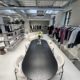 A modern showroom in London with polished concrete floors, featuring a long black table and six chairs, a white sofa, and rails displaying neatly arranged clothing along the bright, minimalist space with large windows.