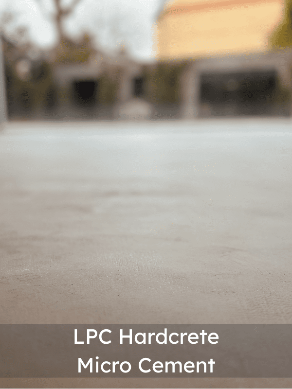 A smooth, light grey microcement surface pictured outdoors, with a blurred background of trees and a building. The text at the bottom reads: LPC Hardcrete Micro Cement.