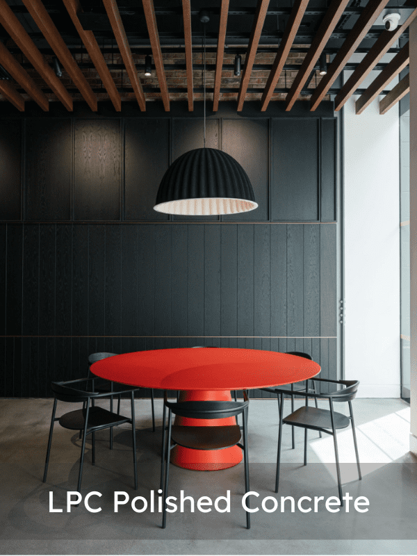A modern room with a round red table, six black chairs, a large black pendant lamp, black wood panelled walls, exposed ceiling beams, and LPC Polished Concrete text overlay at the bottom.