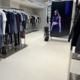 A modern clothes shop interior with rails of neatly arranged clothes, a golf bag, and a large digital screen displaying a model in a black crop top and sunglasses walking on a catwalk.